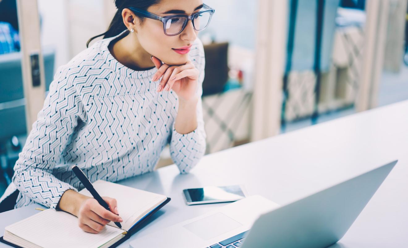 Woman reading publications on laptop and taking notes